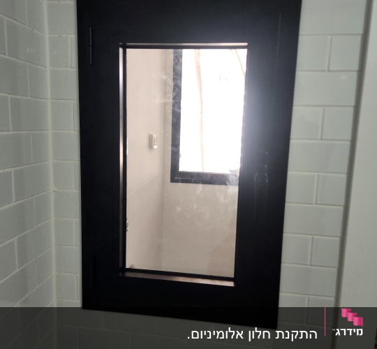 חלון אלומיניום שחור על קיר אריחים לבנים